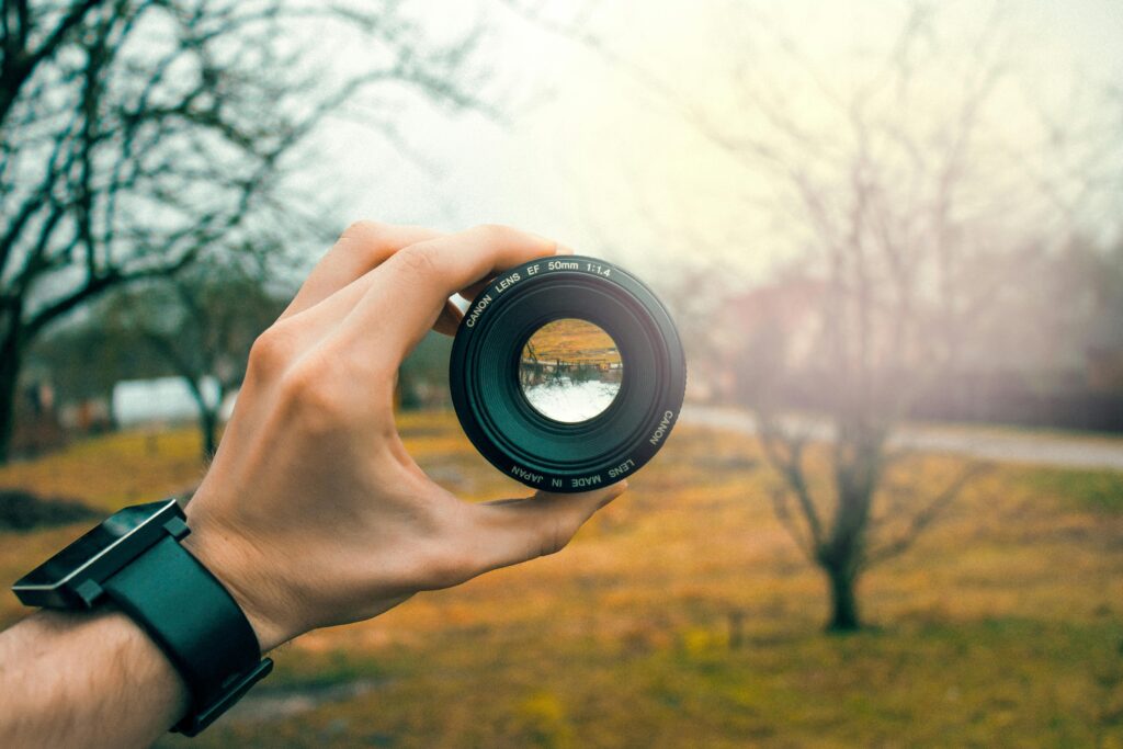 Close-up of a hand holding a 50mm camera lens outdoors, focusing through the lens.